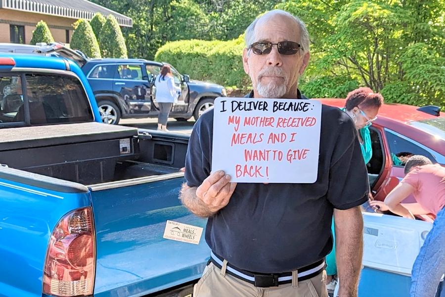 50th Anniversary: man holding sign that says "I deliver because my mother recieved meals and I want to give back."